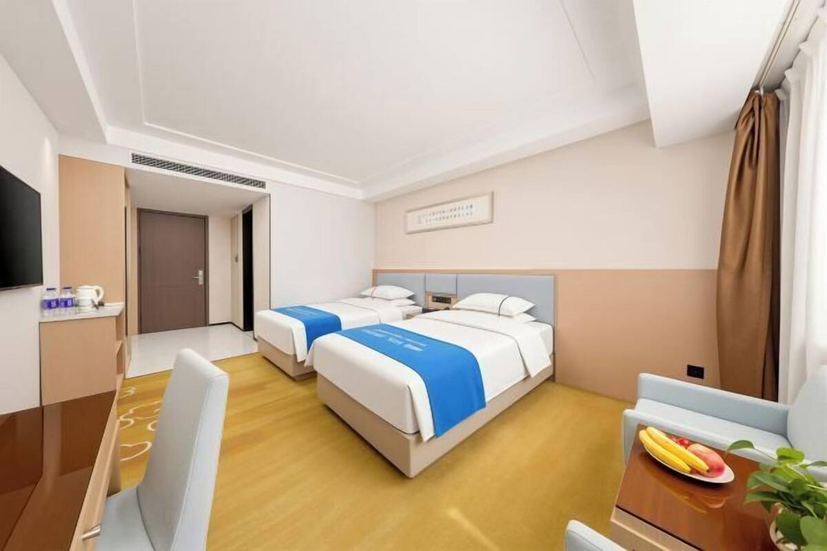 Ein Hotelzimmer mit zwei Betten, einem Schreibtisch, einem Stuhl, einem Fernseher und einem kleinen Tisch mit Obst.