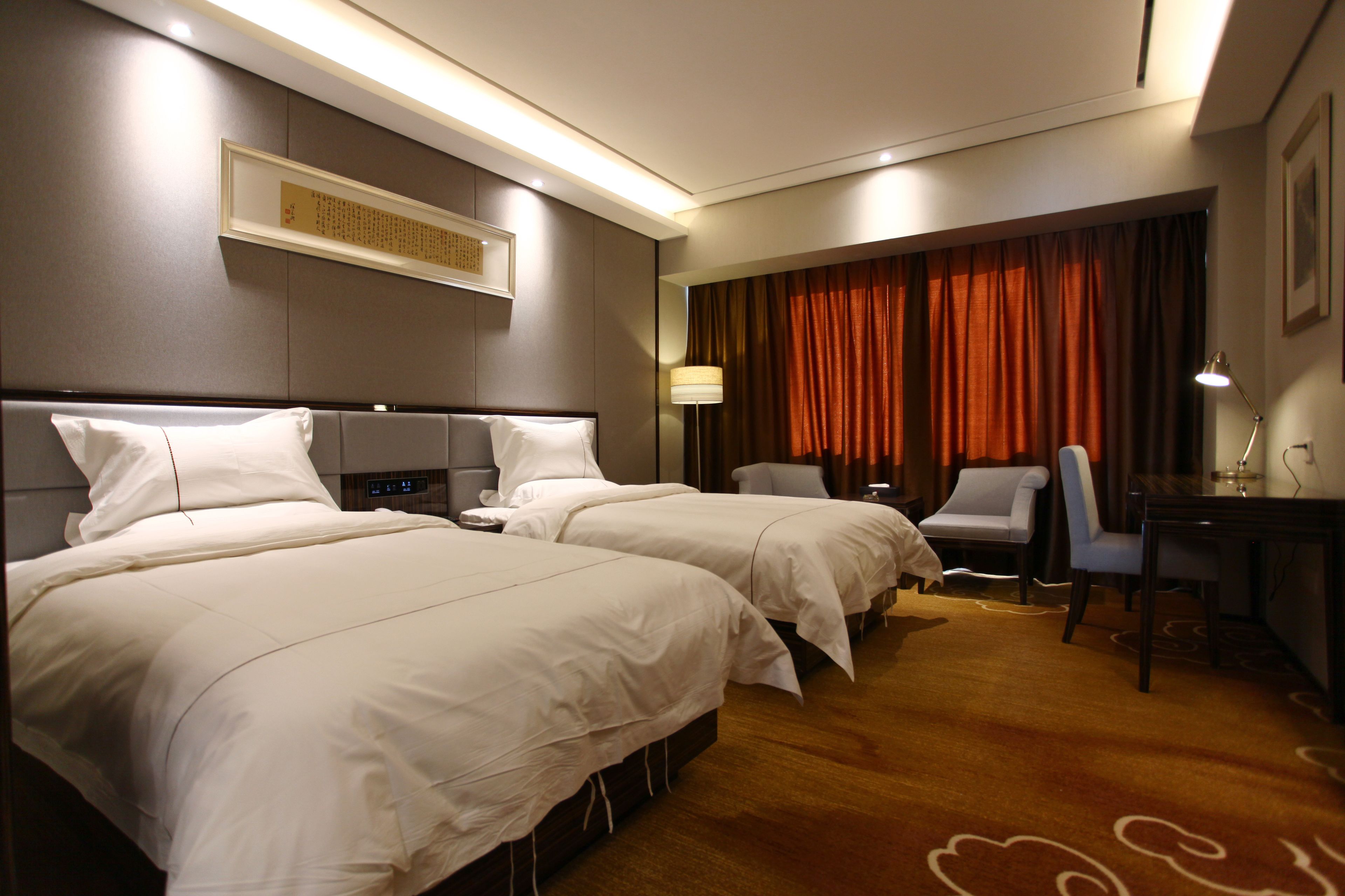 Ein Hotelzimmer mit zwei Betten, einem Schreibtisch, einem Stuhl und einem großen Fenster mit Vorhängen.