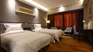 Ein Hotelzimmer mit zwei Betten, einem Schreibtisch, einem Stuhl und einem großen Fenster mit Vorhängen.