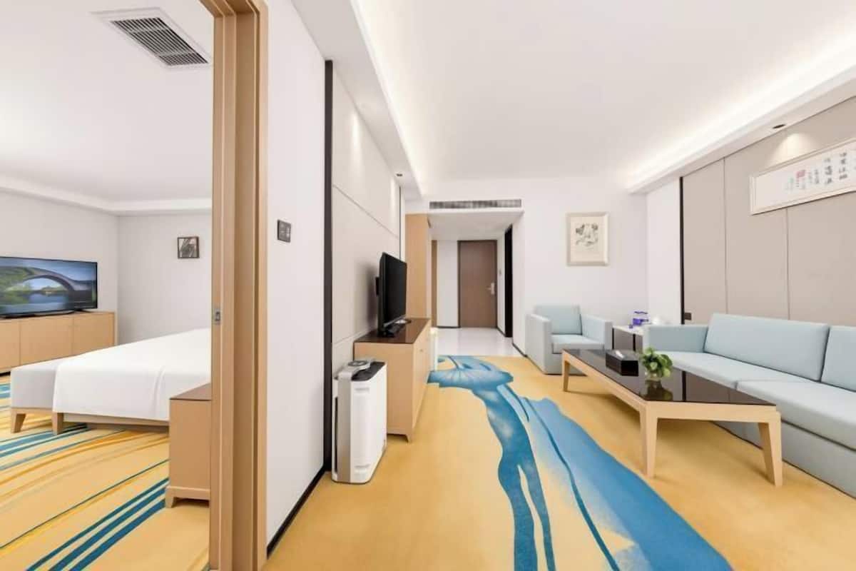 Ein Hotelzimmer mit Bett, Fernseher, Sofa, Couchtisch und einem an der Wand befestigten Fernseher.