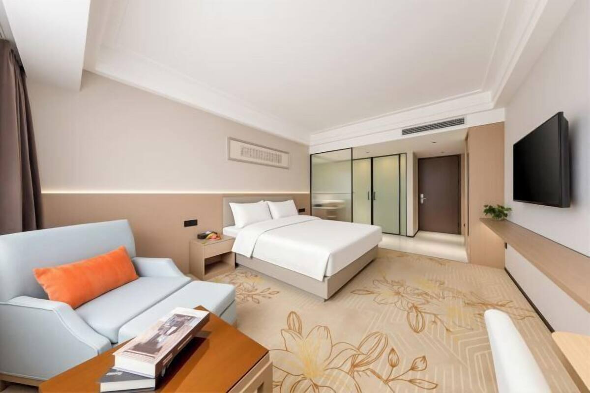 Ein Hotelzimmer mit Bett, einer Couch, einem Fernseher, einem Nachttisch und einem Kleiderschrank.