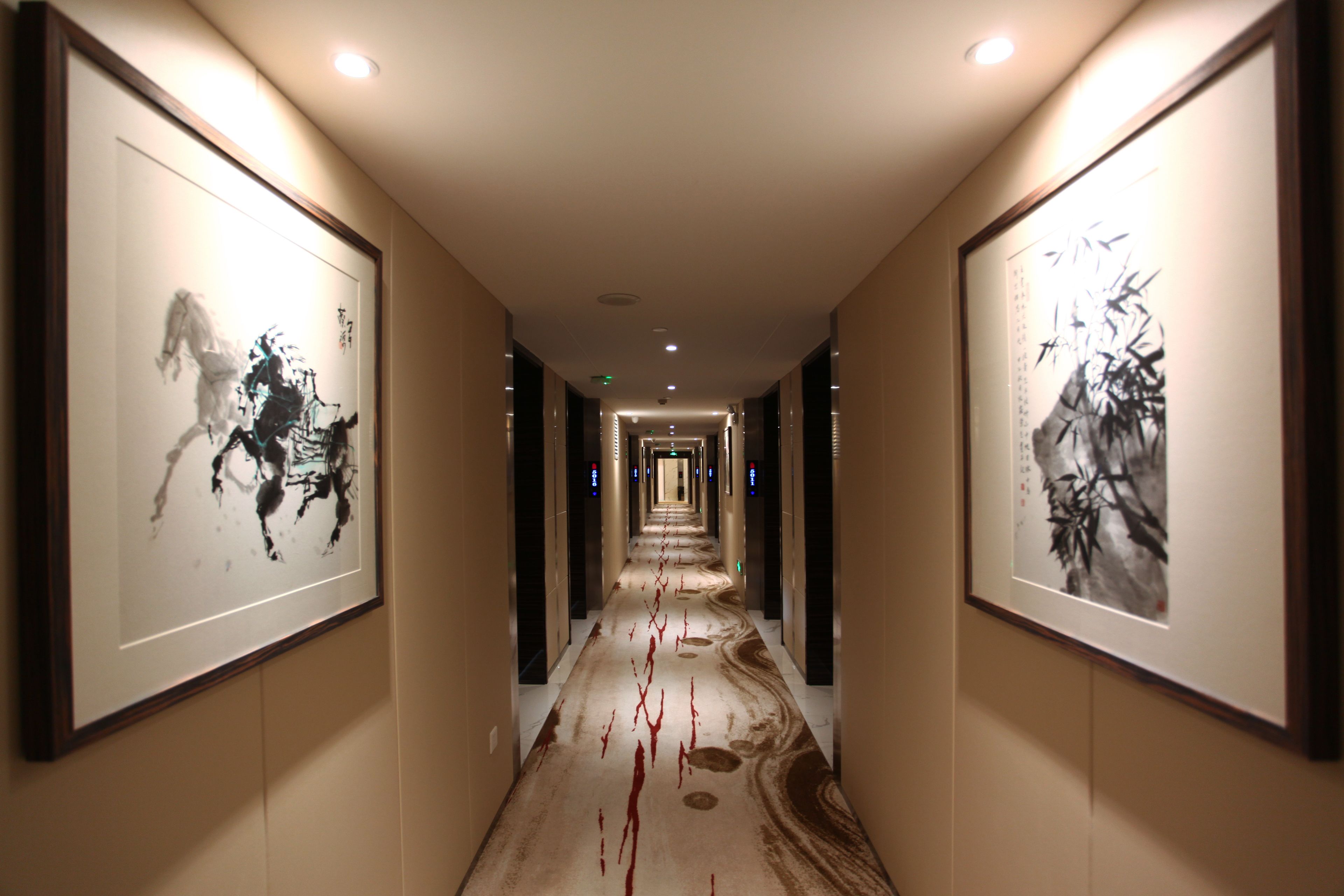 Un pasillo con cuadros enmarcados en las paredes, alfombra estampada y una serie de puertas que dan a varias habitaciones.