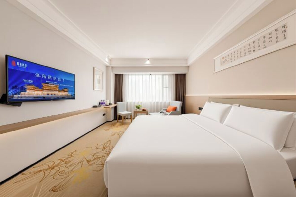 A hotel room with a large bed, a desk with a chair, a television mounted on the wall, and a window with curtains.
