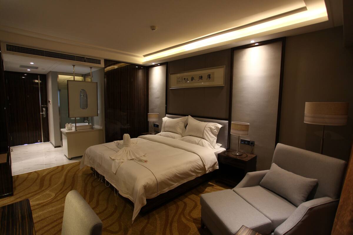 Ein Hotelzimmer mit einem großen Bett, einer Sitzecke, einem Nachttisch mit Lampe und einem Spiegel.