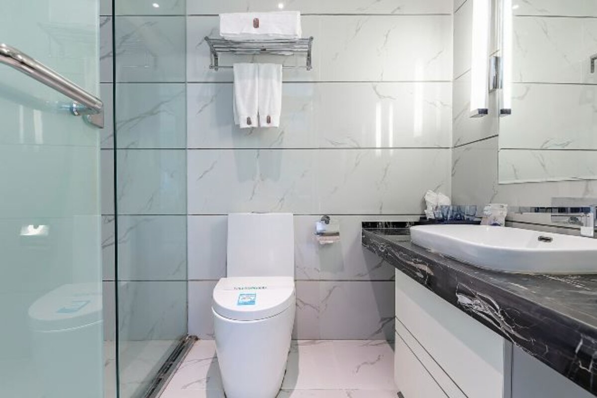 A modern bathroom with a glass shower enclosure, a white toilet, a marble-tiled wall, and a black countertop with a sink.