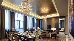 A spacious hotel room with a large dining table, comfortable seating, a chandelier, and a television. - Wanda Realm Dongying (Dongying)