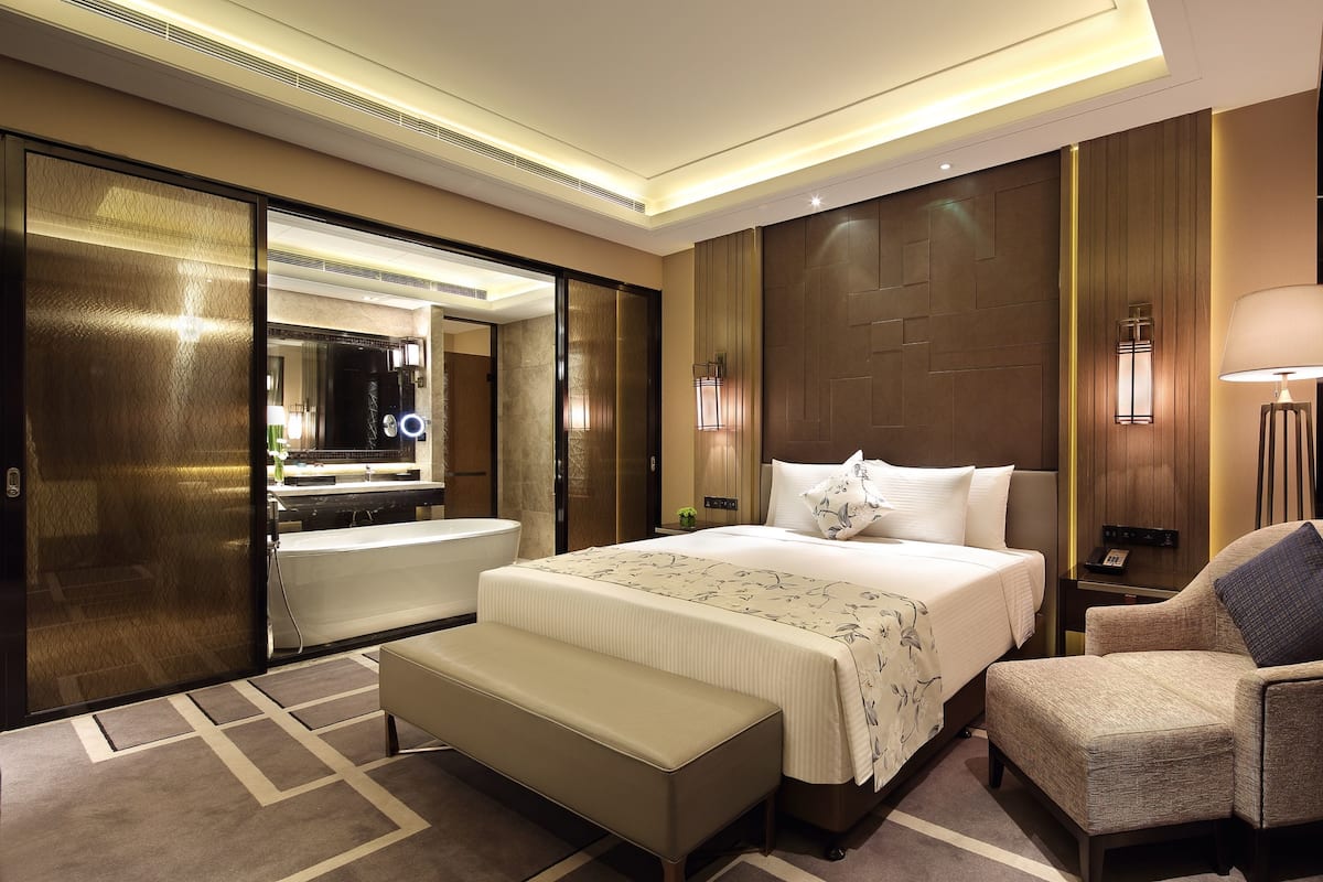 A hotel room with a large bed, a sitting area, a bathroom, and a mirror.