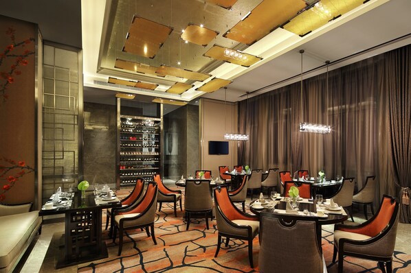 Un comedor de hotel con varias mesas, sillas y una estantería para vinos.