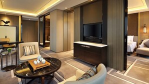 A modern hotel room with a flat-screen TV, a sofa, a coffee table with decorative items, and a dining area with a table and chairs. - Wanda Realm Dongying (Dongying)