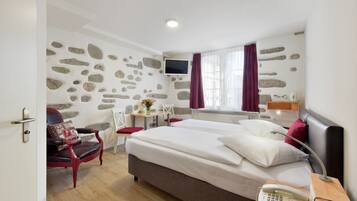 Quarto de hotel com cama grande, escrivaninha, cadeira, televisão e parede de pedra.