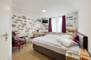 Quarto de hotel com cama grande, escrivaninha, cadeira, televisão e parede de pedra.