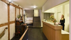 Zona de recepción con mostrador de madera, un banco y una escalera al fondo.