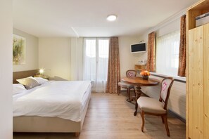 A hotel room with a bed, a desk with a chair, a TV, and a window with curtains.