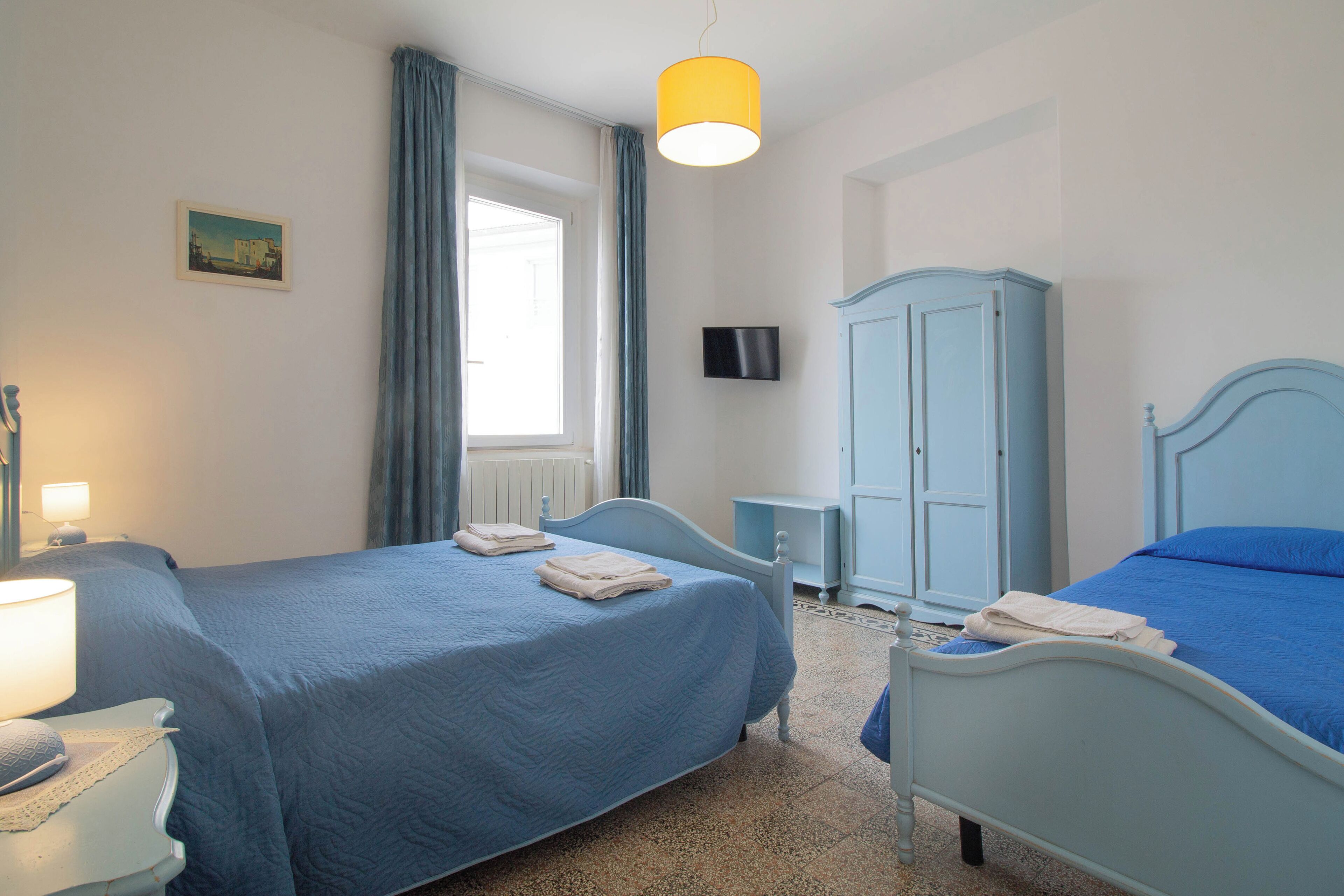 Ein Schlafzimmer mit zwei Betten, einem Kleiderschrank, einem Fernseher und einem Fenster mit Vorhängen.