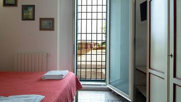 Una habitación de hotel con una cama, un radiador, una puerta con vistas y suelo de baldosas.