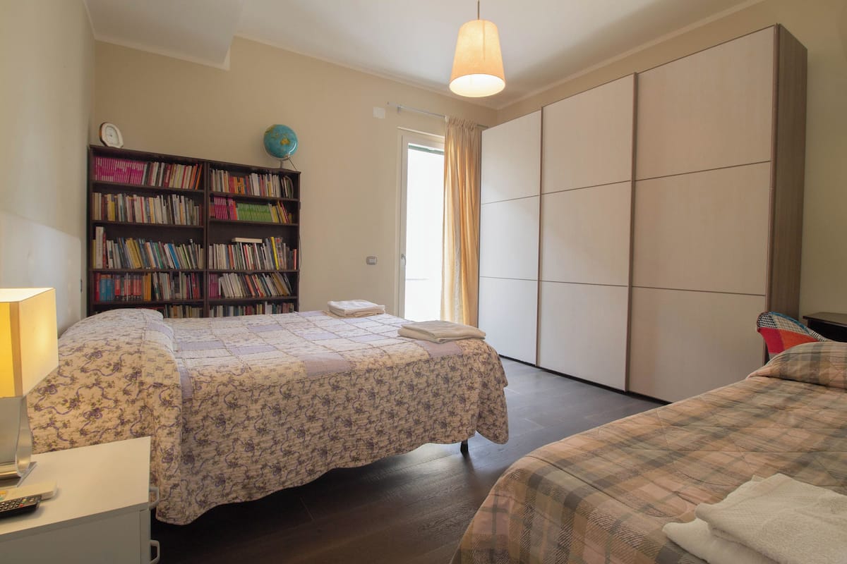 A bedroom with two beds, a bookshelf, a desk with a lamp, and a wardrobe.
