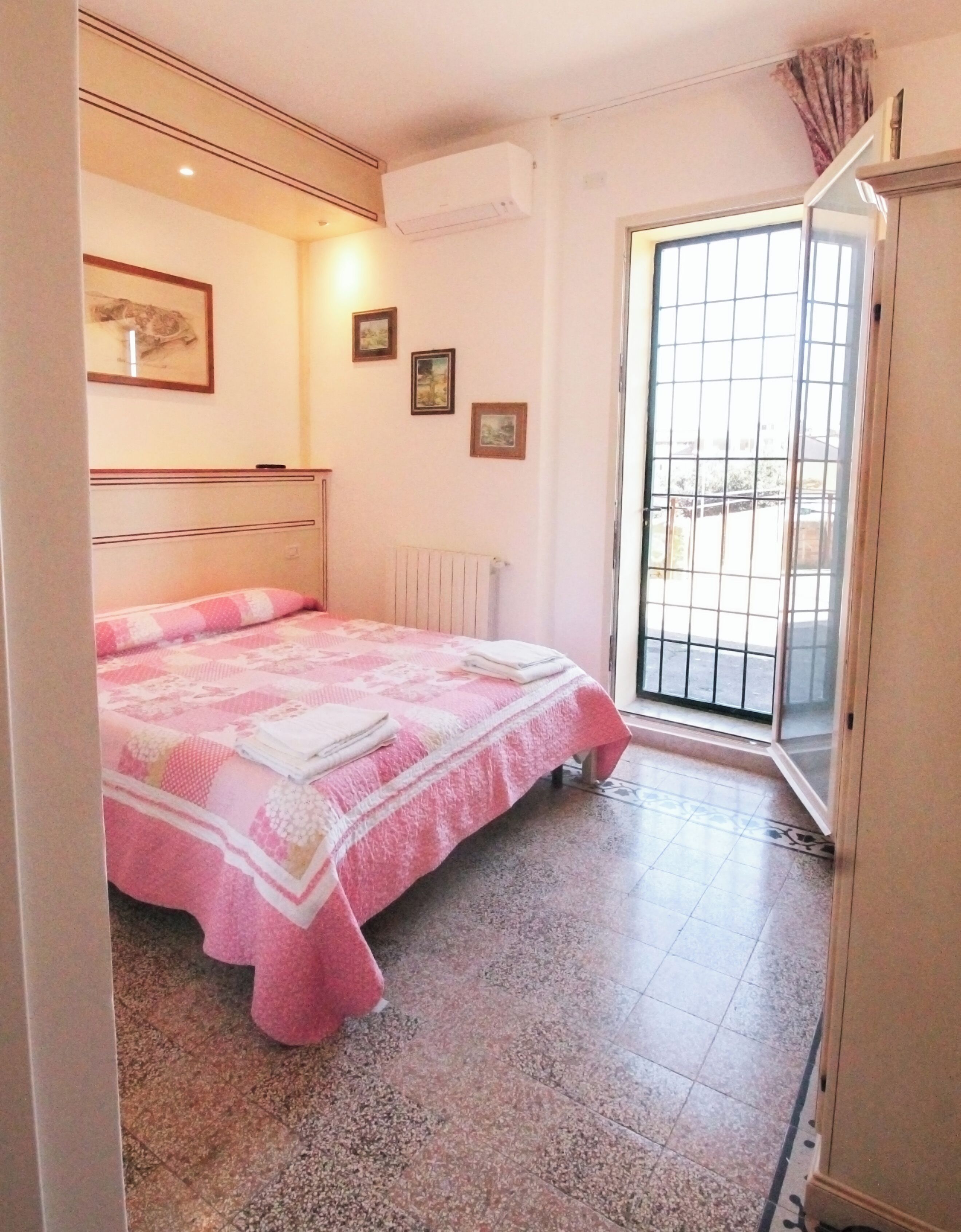 A bedroom with a bed, a radiator, a window with a view, and a door.