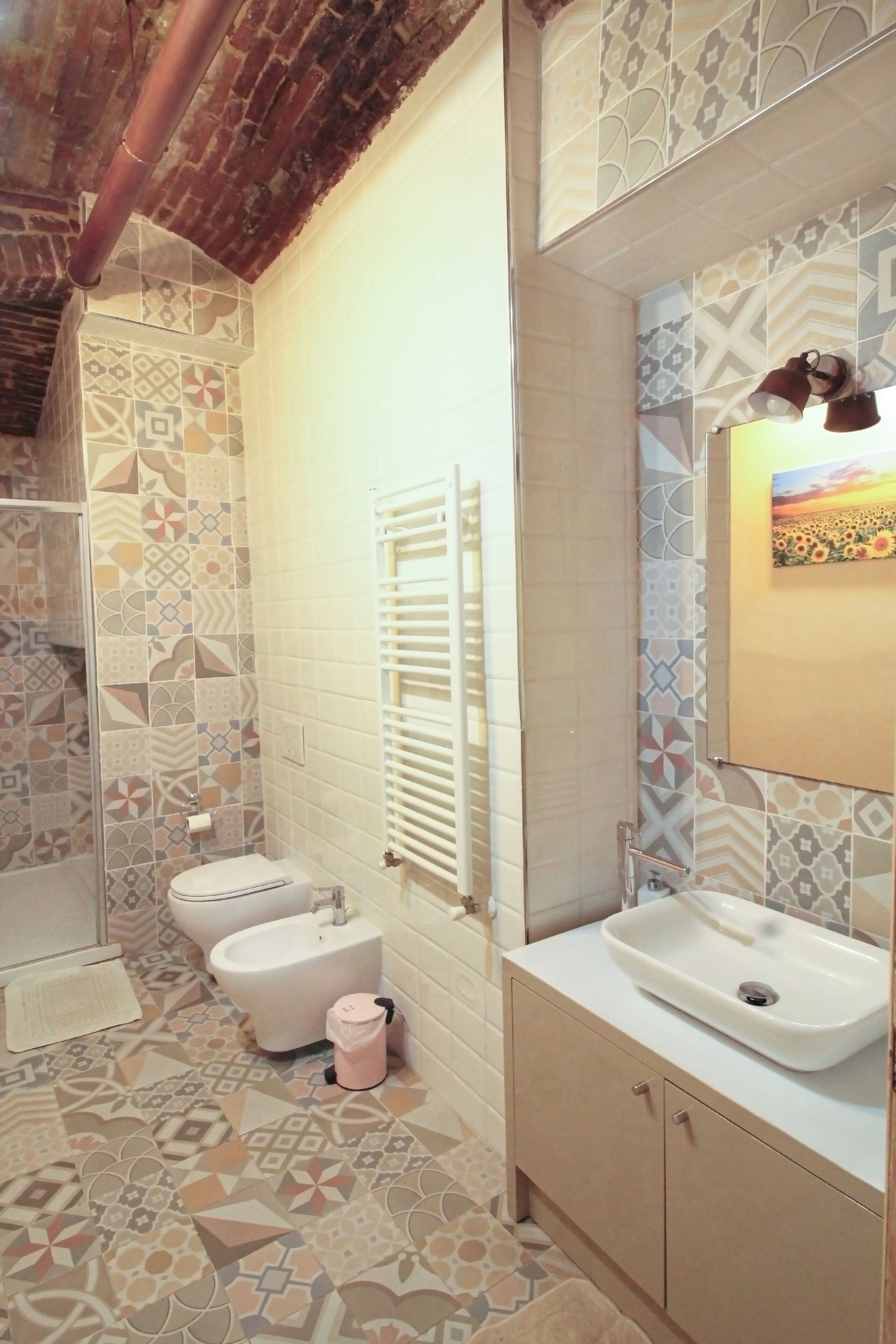 Un baño con baldosas estampadas, un inodoro blanco, un bidé, un lavamanos y un perchero para toallas.