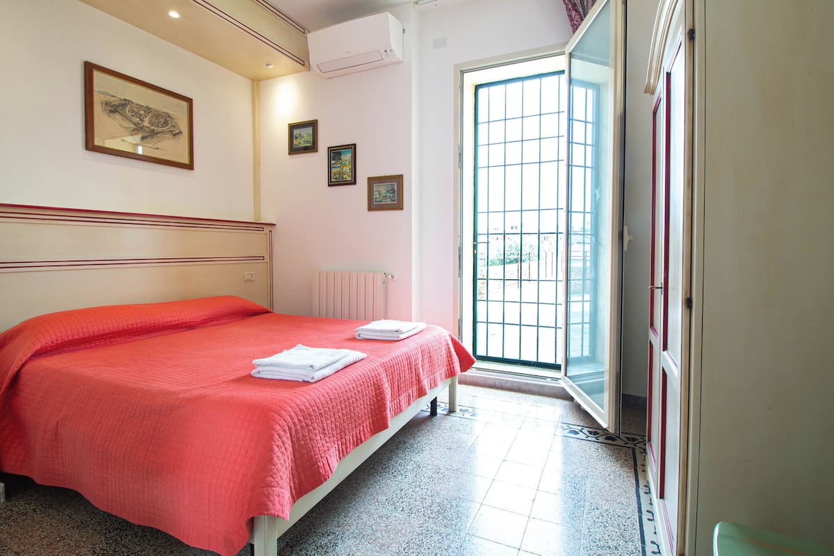 A hotel room with a bed, a radiator, a door with a glass panel, and a framed picture on the wall.
