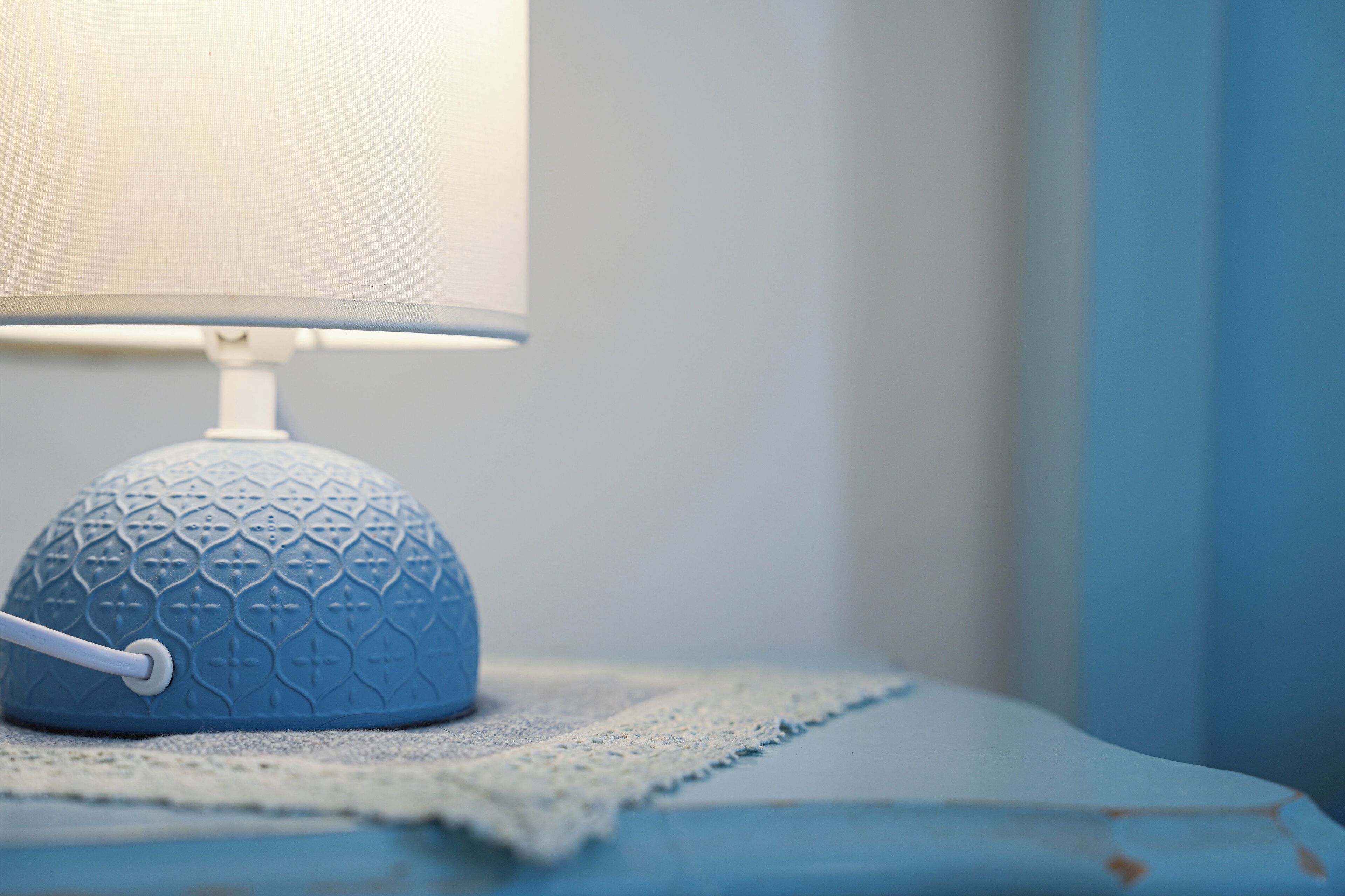 A blue textured lamp on a bedside table with a lace doily.