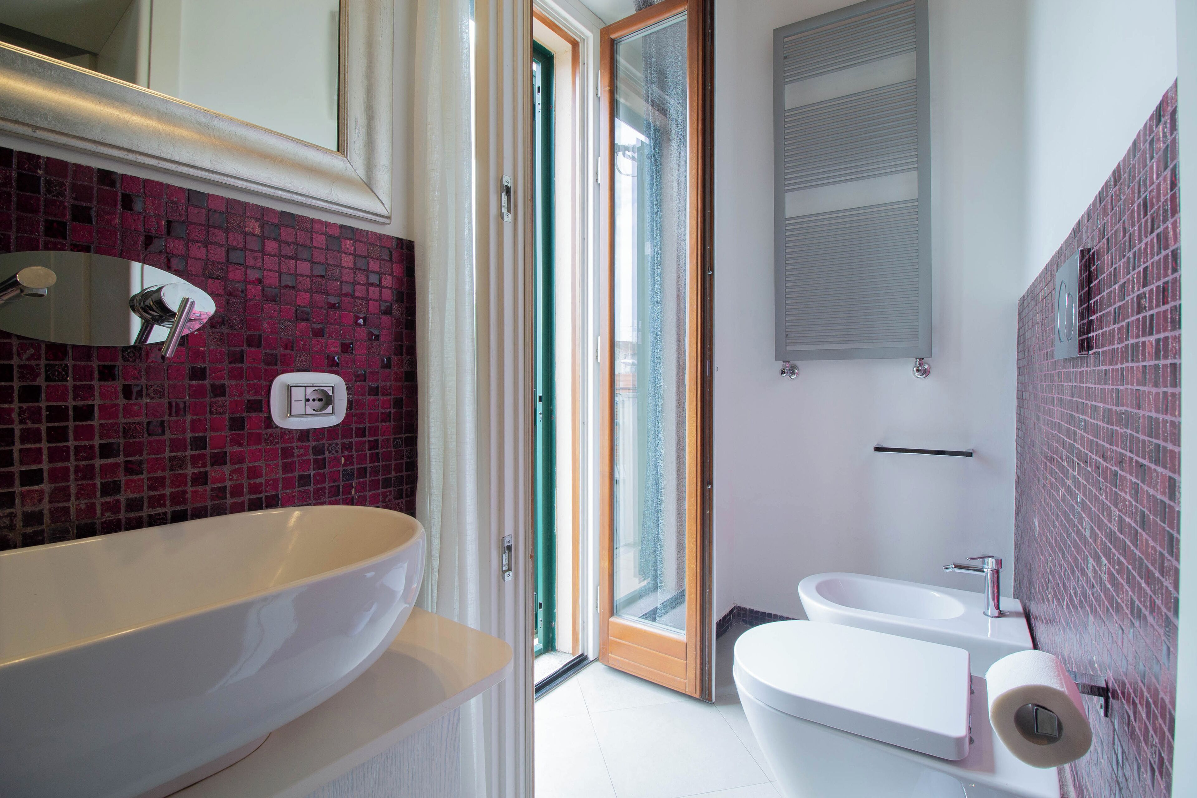 Une salle de bain avec une grande baignoire blanche, un lavabo blanc et des toilettes. Une porte en verre donne accès à un balcon.