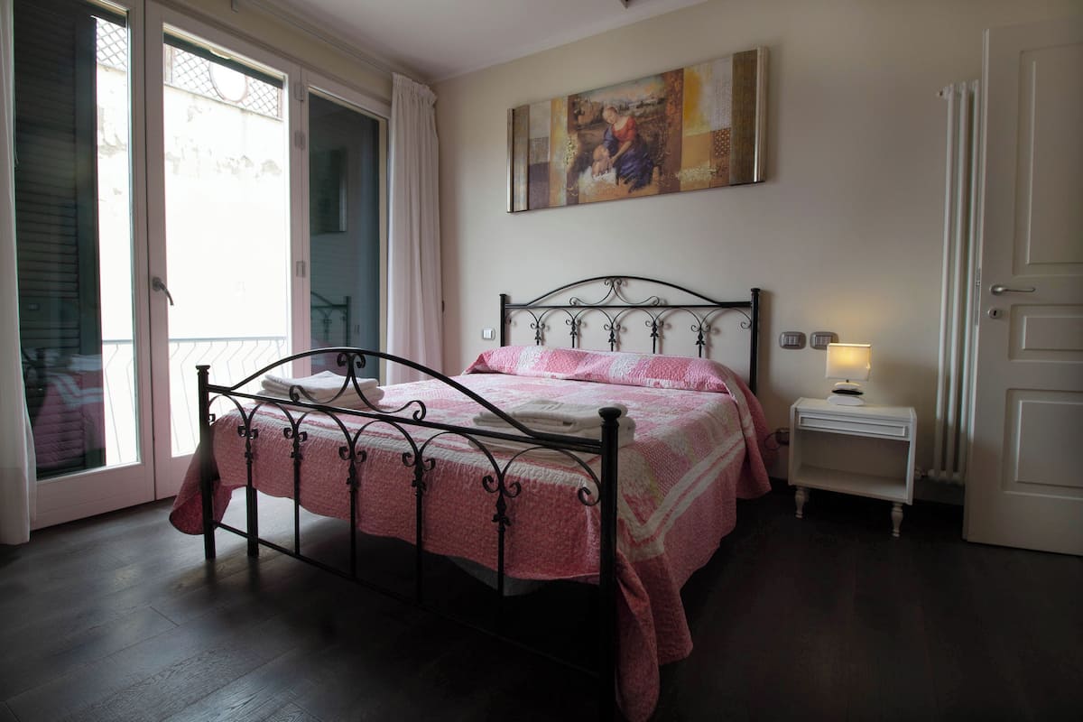 A bedroom with a metal bed frame, a bedside table with a lamp, and a window with curtains.