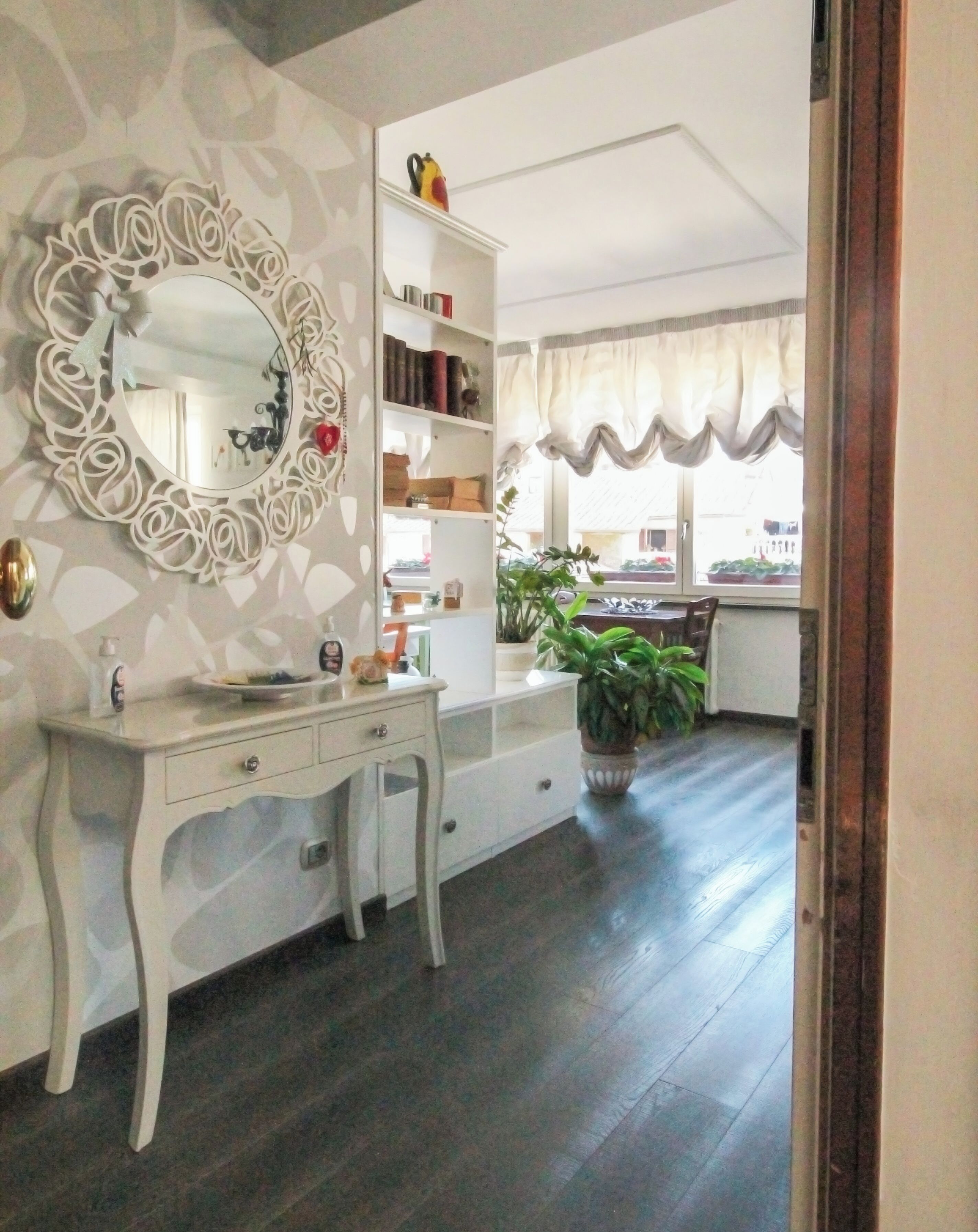 A room with a white vanity, a mirror with a decorative frame, a bookshelf, and a potted plant.