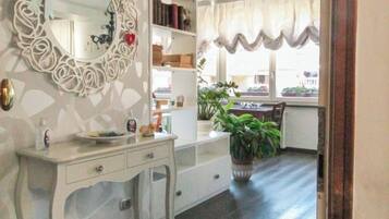 A room with a white vanity, a mirror with a decorative frame, a bookshelf, and a potted plant.