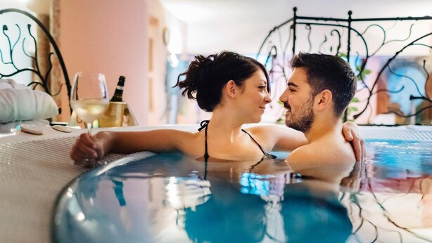 A couple in a hot tub with a laptop and a bottle of wine on the side.