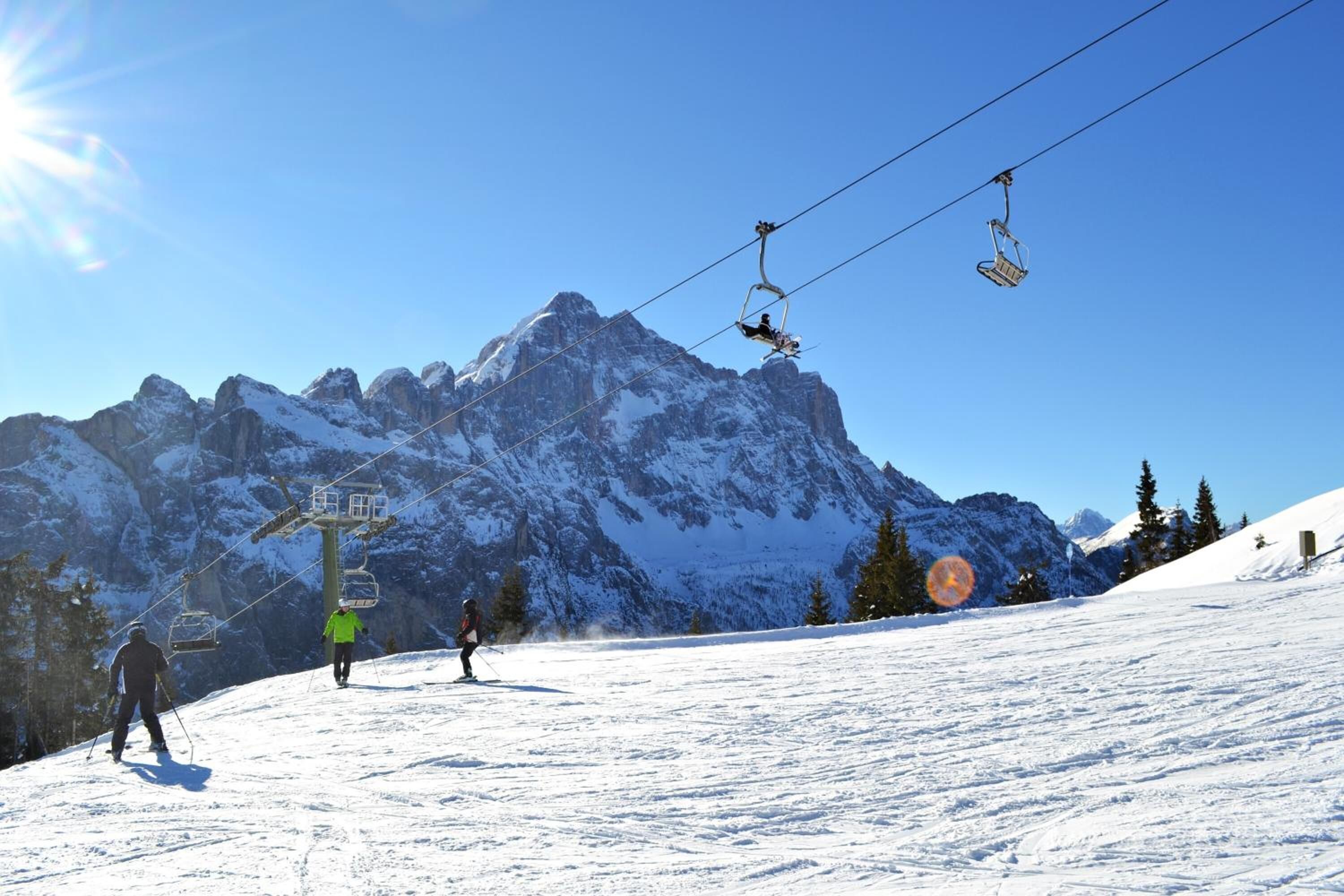 Une piste de ski avec un télésiège, des montagnes enneigées et un ciel dégagé.