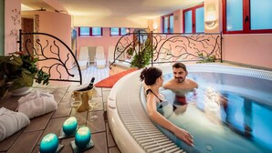 A couple in a hot tub with a decorative metal fence, a small table with a bottle and glasses, and candles on the floor.