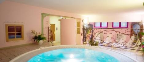 An indoor swimming pool with a hot tub, surrounded by pink walls and decorative elements.