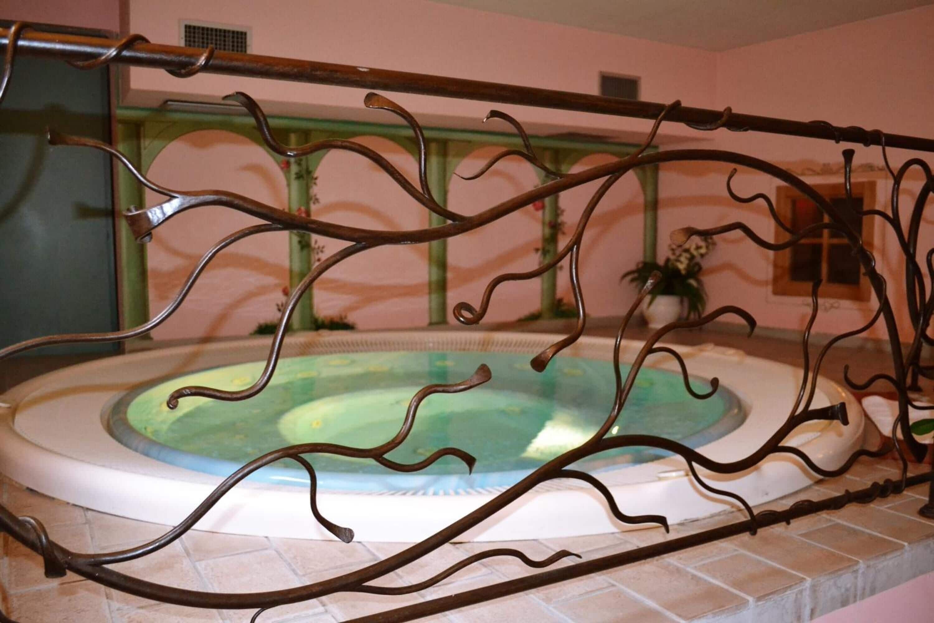 Una vasca idromassaggio con ringhiera decorativa in metallo, circondata da un pavimento piastrellato e una parete rosa.