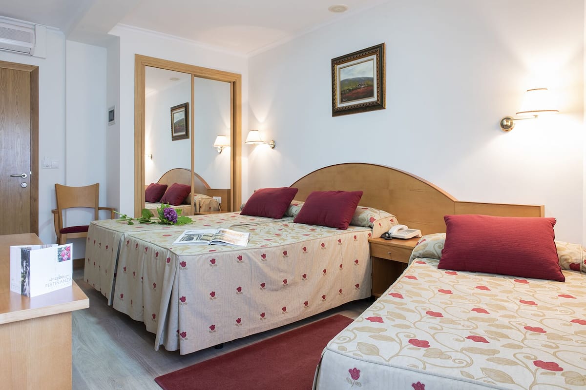 Une chambre d’hôtel avec deux lits, un bureau en bois, une chaise, un miroir et un tableau encadré au mur.