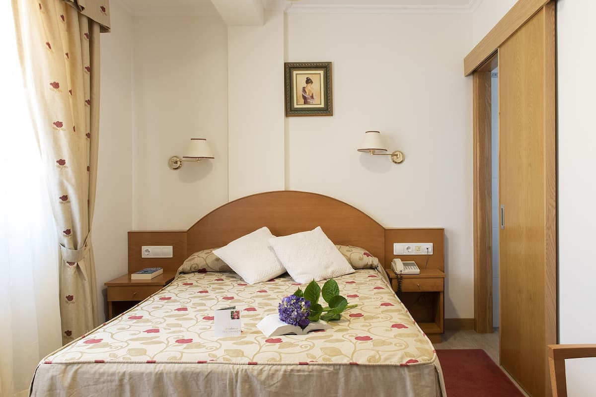 Une chambre d’hôtel bien rangée, avec un lit, des tables de chevet, une petite table d’appoint, une lampe, un tableau encadré au mur et une porte.