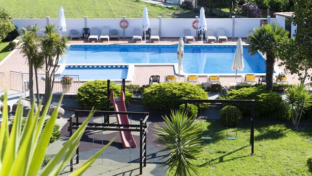 Piscina con tumbonas y un tobogán, rodeada de vegetación y un flotador salvavidas.