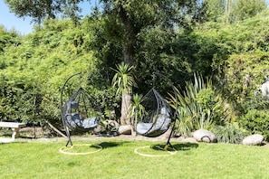 A garden with two hanging chairs, a stone bench, and a variety of plants. - Hotel Cabo Festiñanza (Sanxenxo)