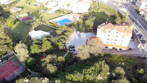 Vista aérea de una zona residencial con piscina, cancha de tenis y un edificio grande con techo rojo.