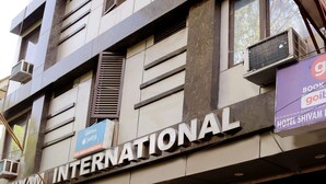 A hotel named Shivam International with a closed shutter, air conditioning units, and a signboard advertising a GoI book. - Hotel Shivam International (New Delhi)