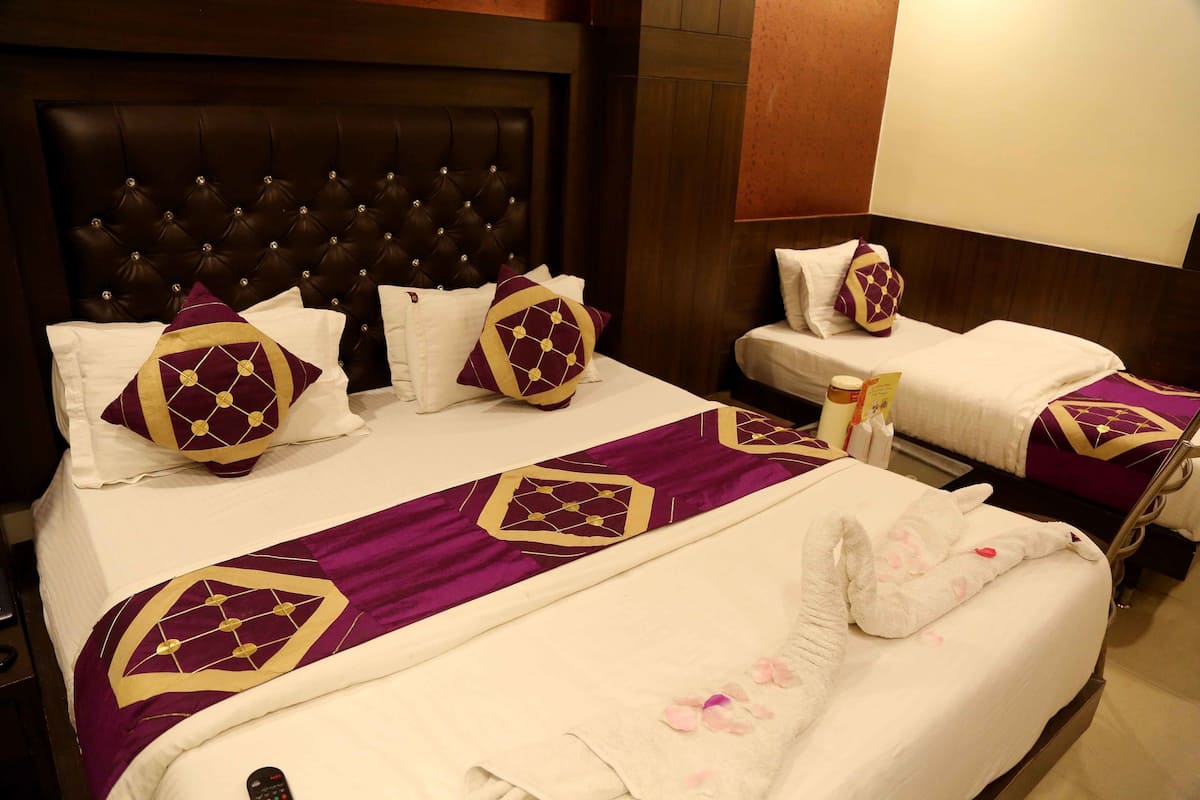 Een hotelkamer met een groot gestoffeerd hoofdbord, twee bedden met passend paars en goud beddengoed, en een witte badruimte.