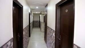 A hallway with dark wooden doors, white walls, and patterned floor tiles. - Hotel Shivam International (New Delhi)