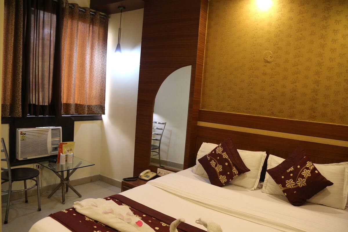 Hotelkamer met een bed, een bureau met stoel, een telefoon en een raam met gordijnen.