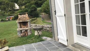 Un patio de piedra con una chimenea de piedra, una puerta blanca y vistas a un paisaje verde con árboles y una montaña.