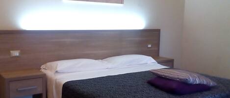 A hotel room with a bed, a nightstand, a drawer, and a wall-mounted artwork.
