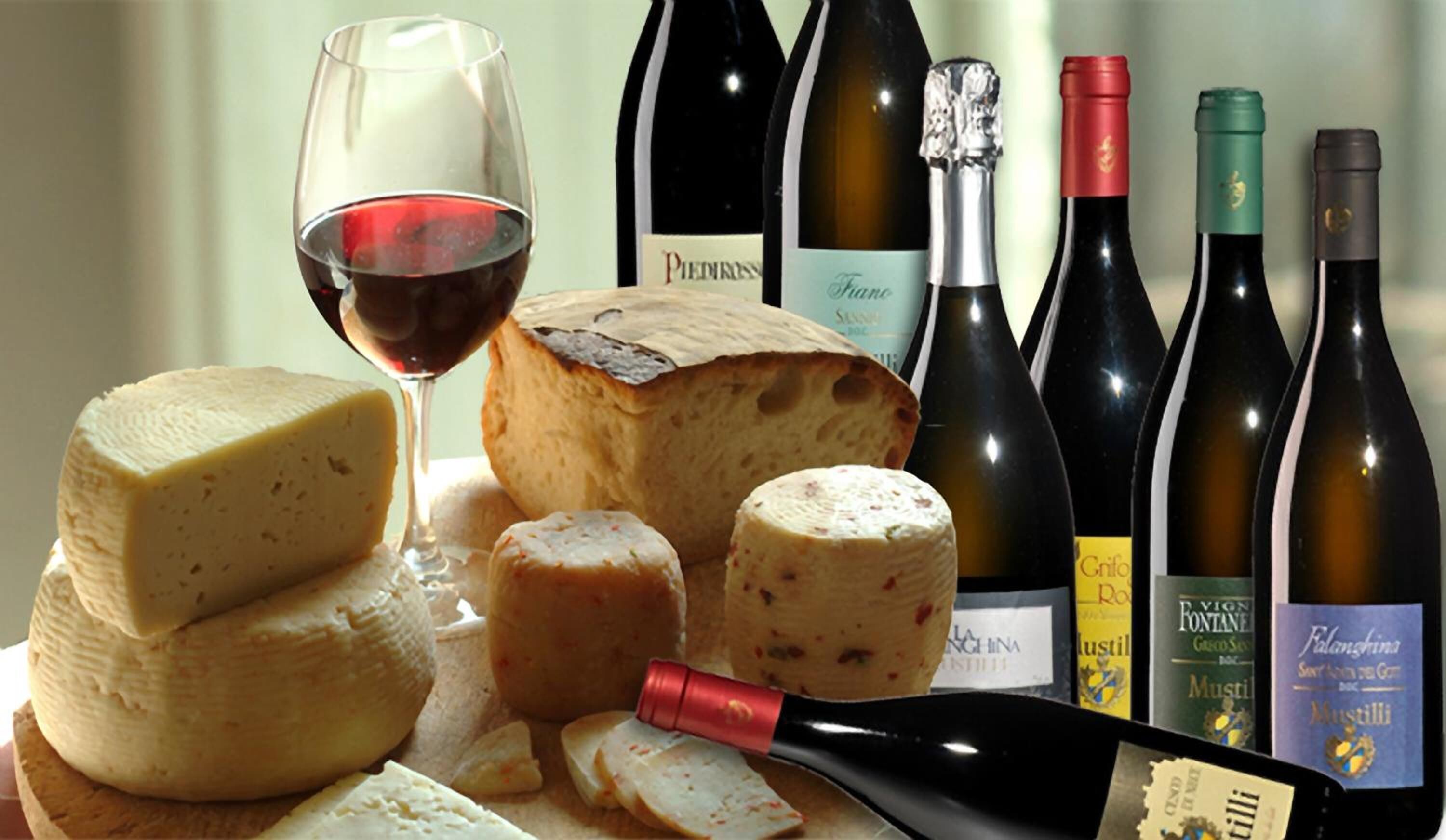 Una variedad de quesos, una copa de vino y varias botellas de vino.