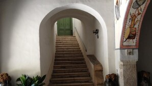 A staircase with a green door at the top, flanked by two potted plants and a wall with a decorative element. - Agriturismo Mustilli (Sant'Agata de'Goti)
