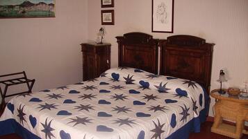 Un dormitorio con una cama grande, una mesita de noche de madera, una silla y cuadros enmarcados en la pared.