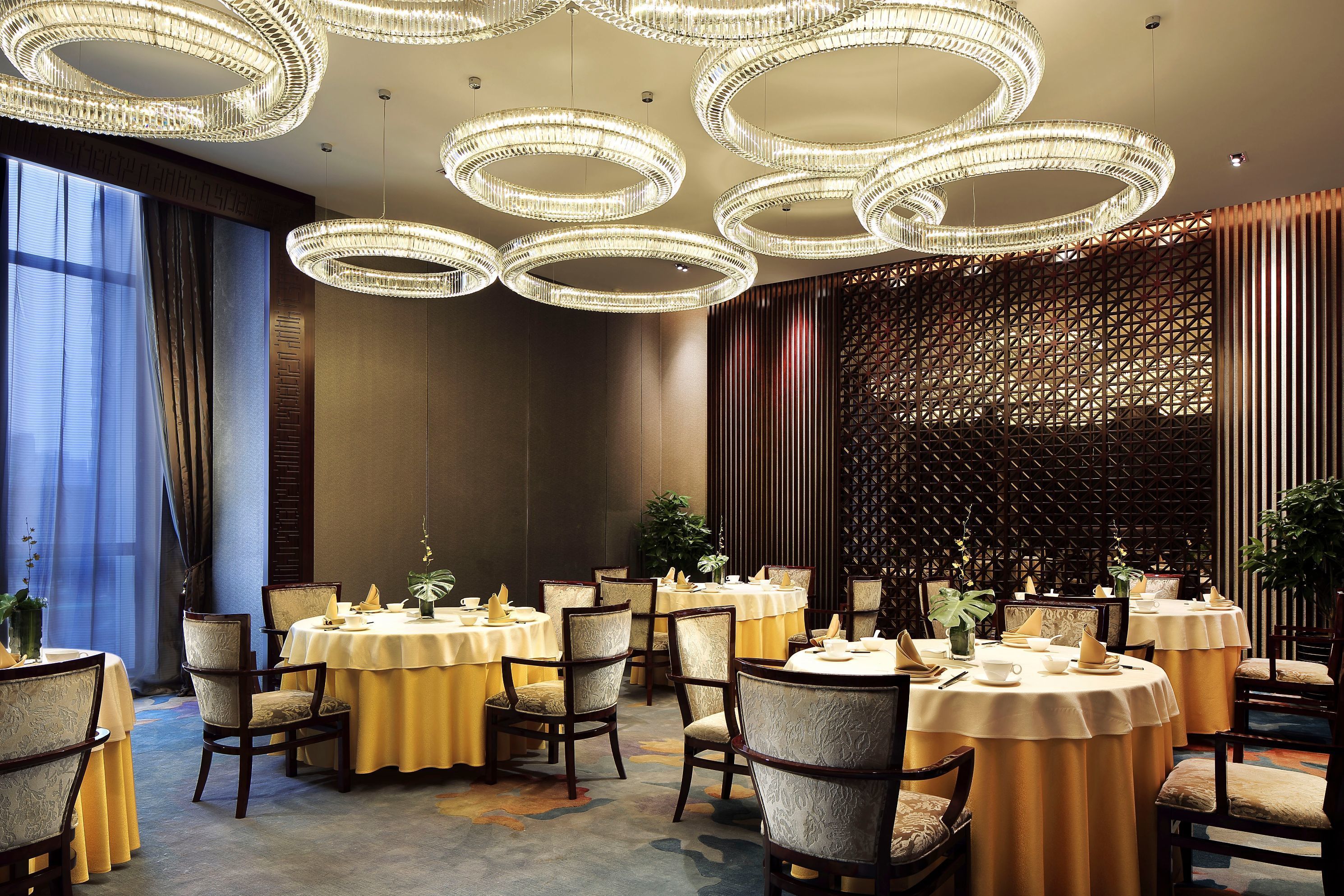 A dining area with round tables, chairs, and chandeliers.