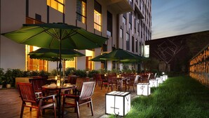 An outdoor patio area with wooden tables and chairs, green umbrellas, and potted plants. - Wanda Realm Anyang (Anyang)