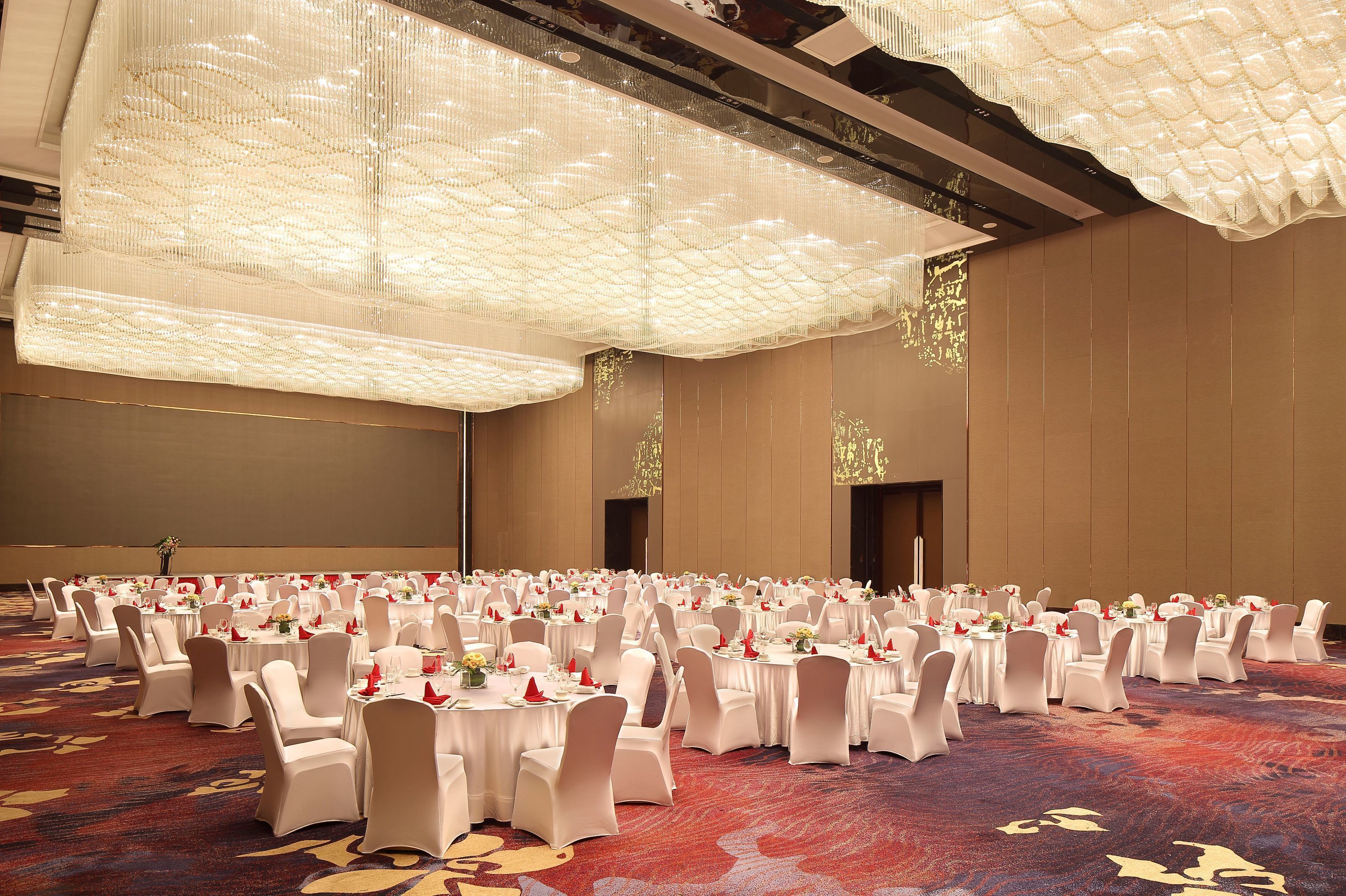 A banquet hall with round tables, white chairs, and a red carpet.